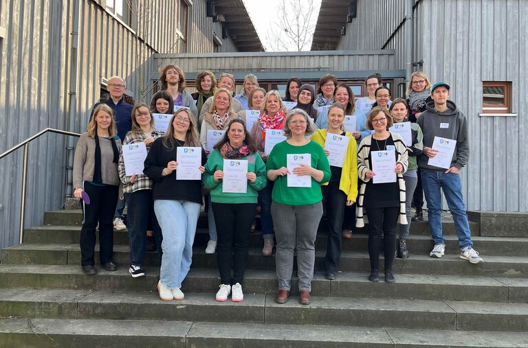 Gruppe von Teilnehmer*innen steht im Innenhof eines Gebäudes und hält ihre Abschlusszertifikate in die Kamera