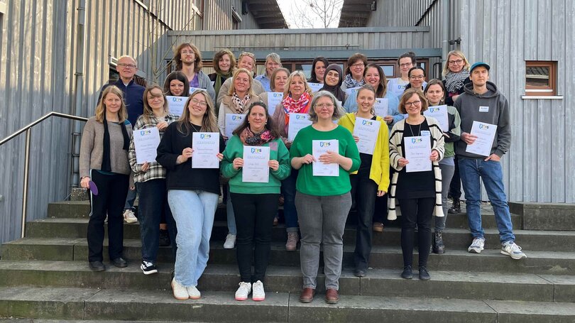 Gruppe von Teilnehmer*innen steht im Innenhof eines Gebäudes und hält ihre Abschlusszertifikate in die Kamera