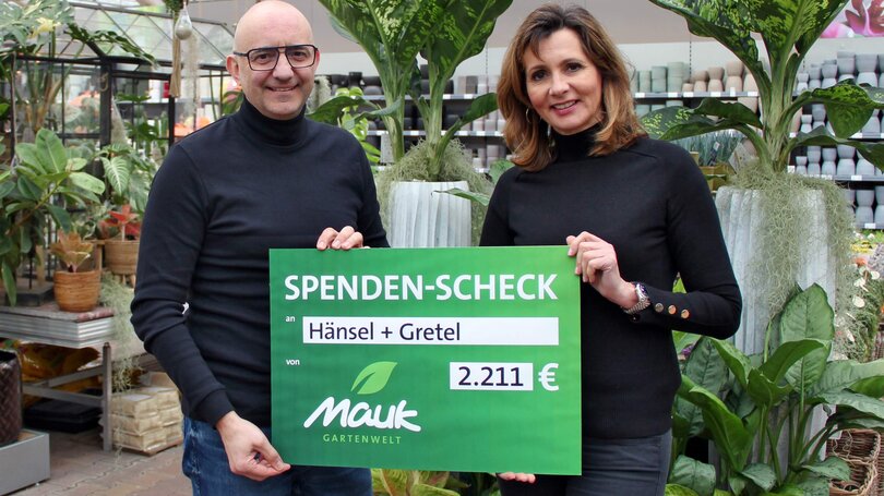 Zwei Personen halten einen Spendenscheck über 2.211 Euro in einem Gartencenter.