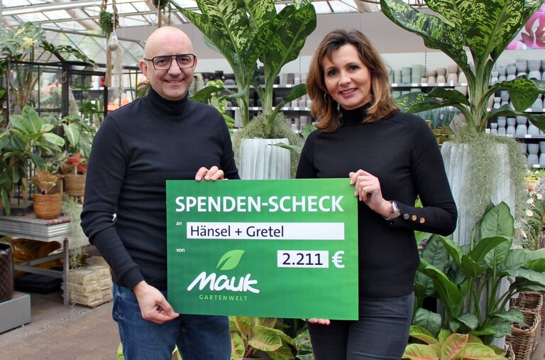 Zwei Personen halten einen Spendenscheck über 2.211 Euro in einem Gartencenter.